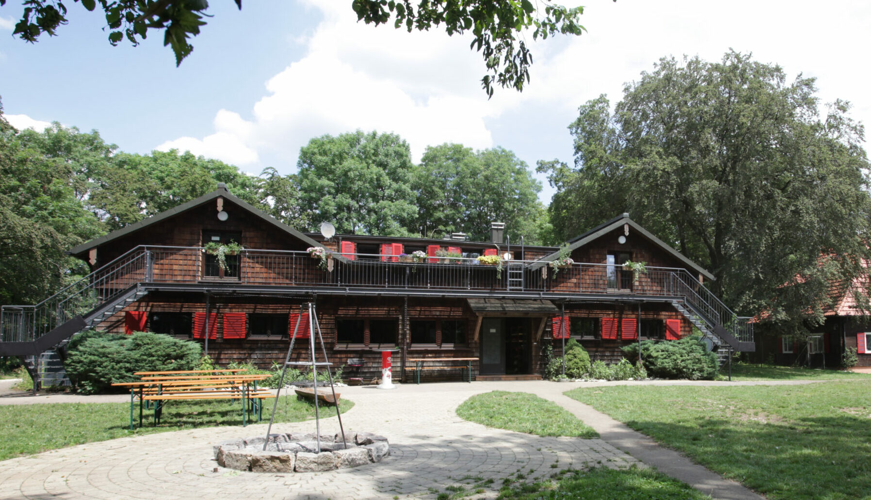 Timber log house with red shutters and a wooden balcony, the Schwarzhornhaus, with a lawn, benches and a fire pit in front