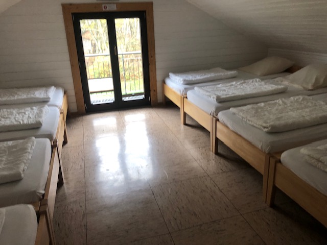 Multi-bed room under the roof with wooden beds and a glass door to a balcony at the Schwarzhornhaus