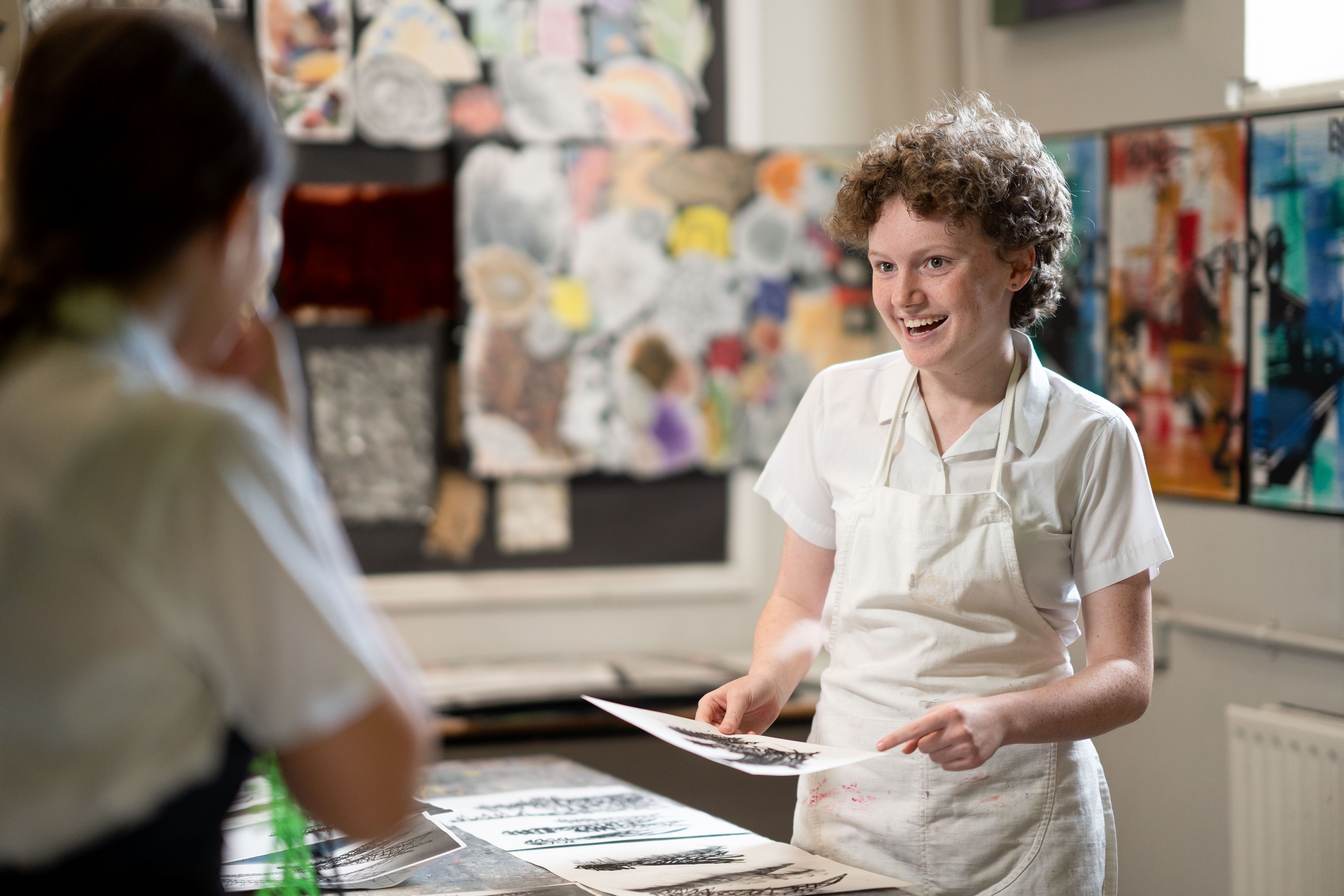 A Cobham Hall pupil in an apron holding a print in the school art room