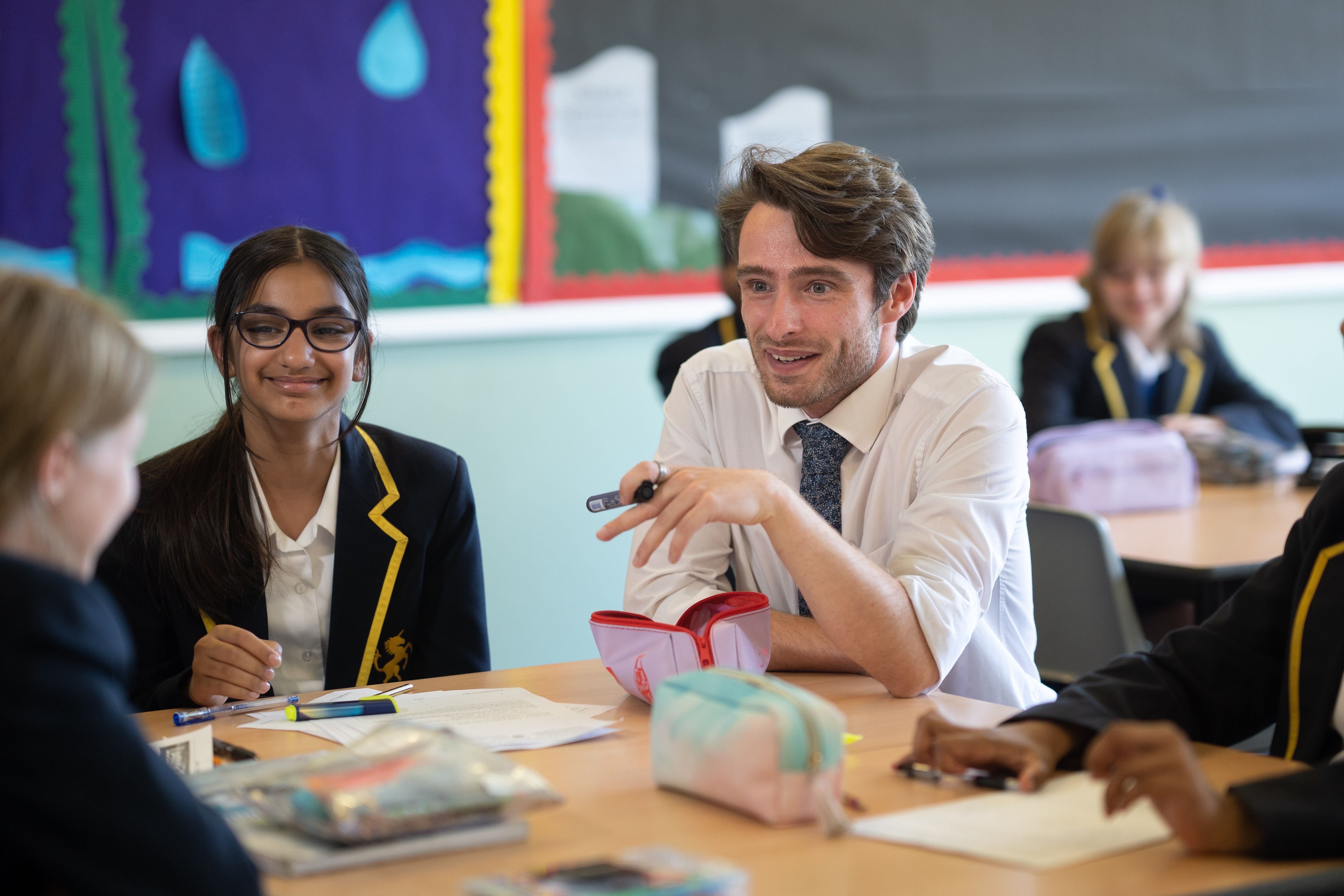 A teacher talking with pupils seated around a classroom table at Cobham Hall