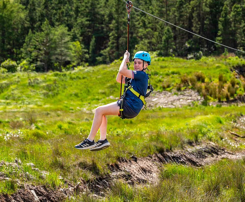 Camper riding the zip line across open green hillside at Delphi Resort
