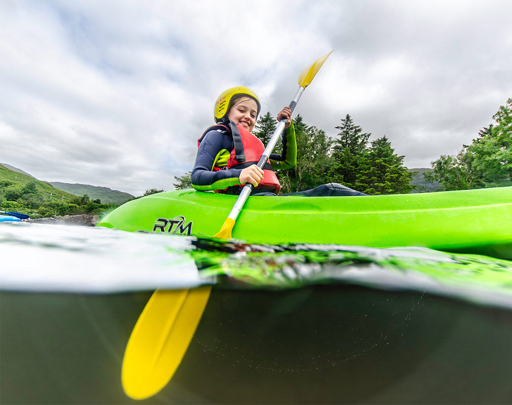 Camper in a helmet and buoyancy aid paddling a kayak on the water at Delphi Resort, Connemara