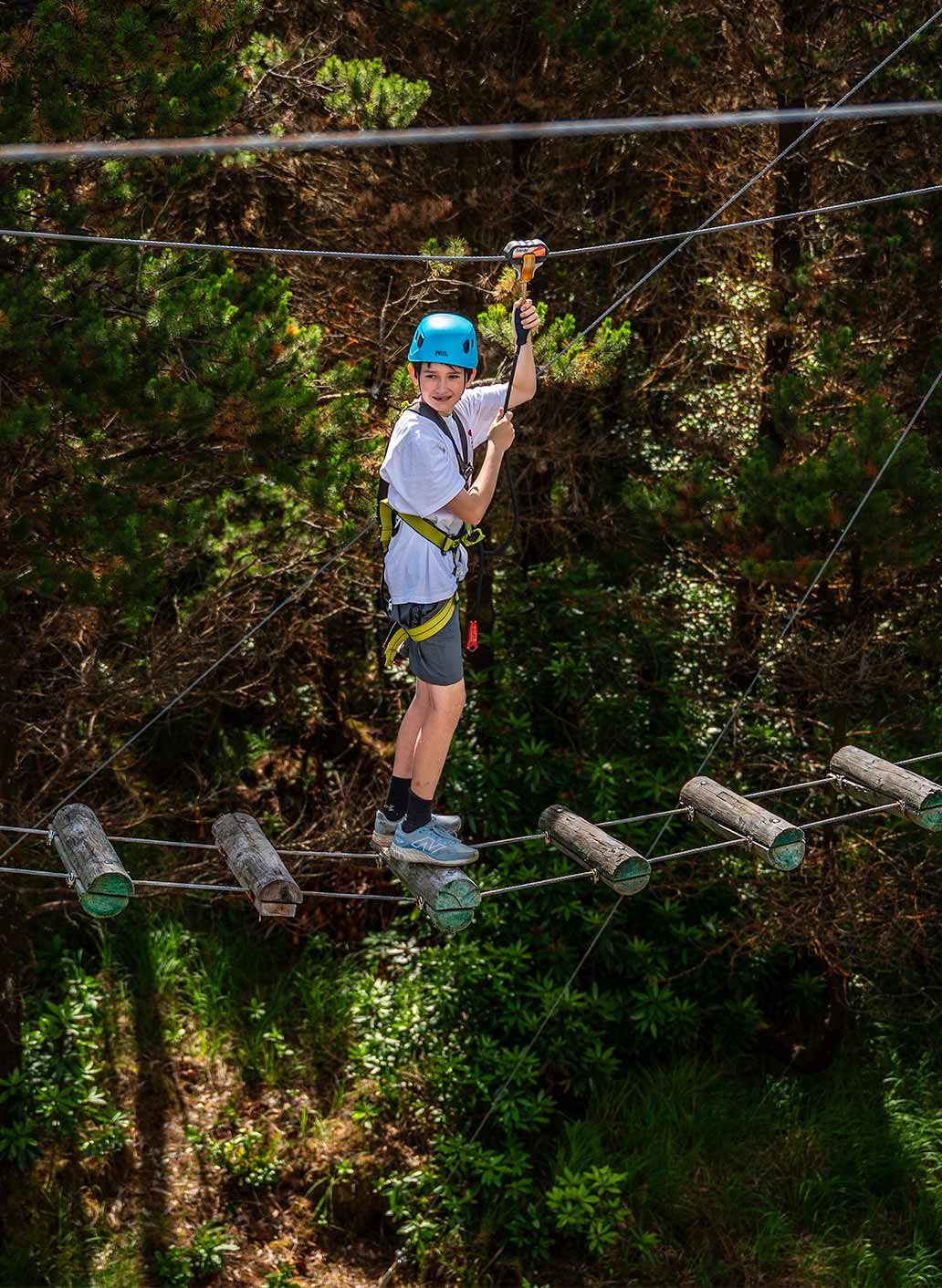 Camper in helmet and harness crossing the aerial trek rope bridge among the trees at Delphi Resort