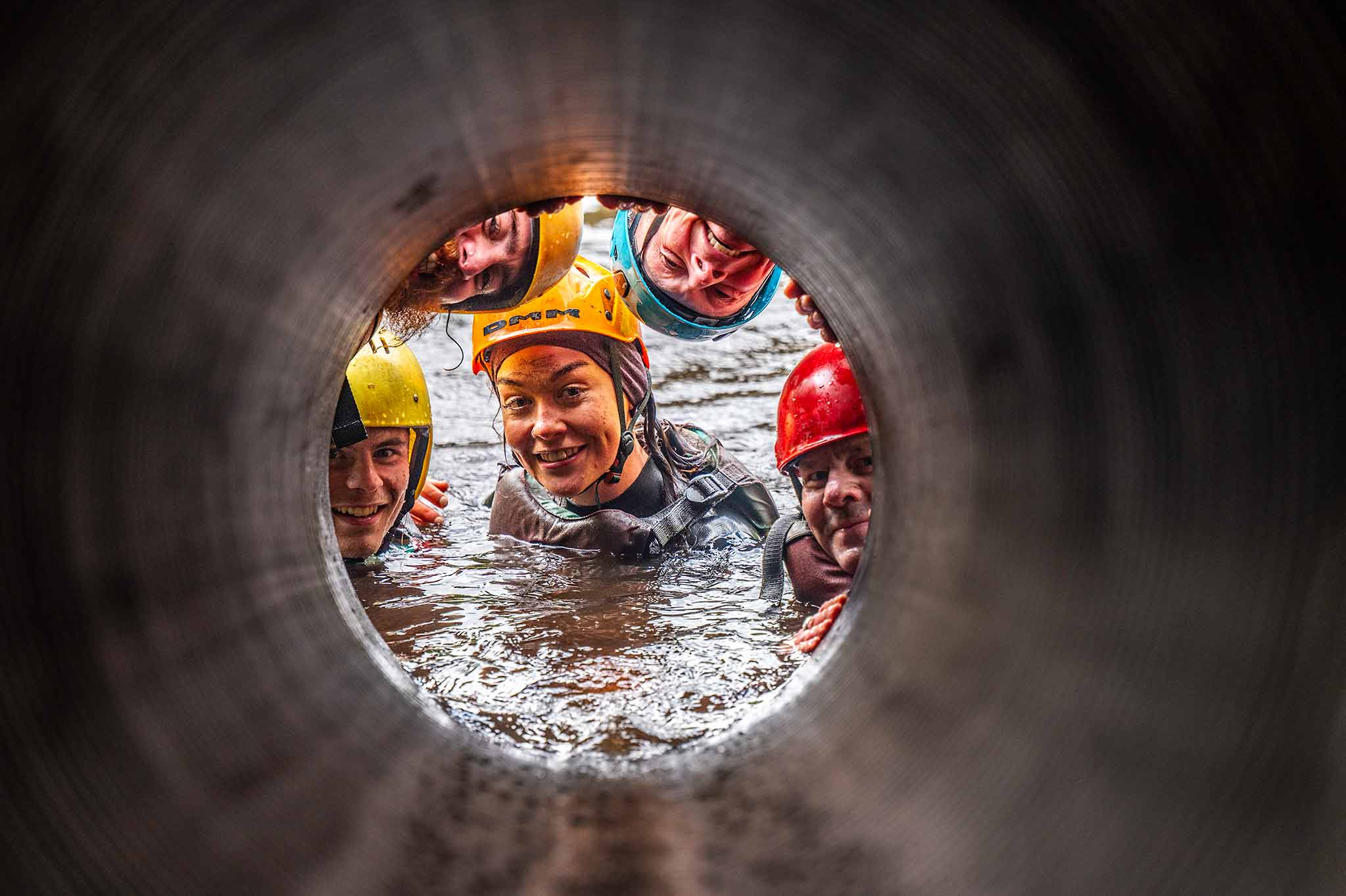 Children in helmets grinning inside a water-filled concrete tunnel on the obstacle course at Delphi Resort