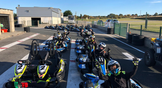 A row of karts lined up in the paddock with young drivers in helmets waiting to start