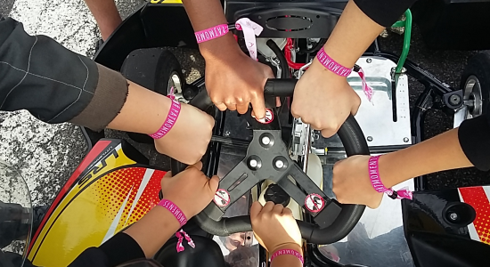 Children’s hands with wristbands gathered on a kart steering wheel before the race