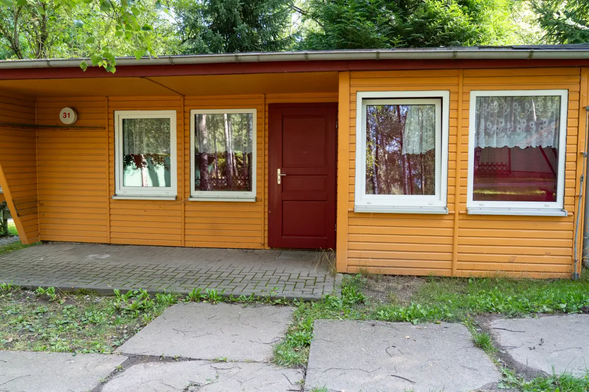 Wooden bungalow with a red door and curtained windows at the Feriendorf Hoher Hain in Limbach-Oberfrohna