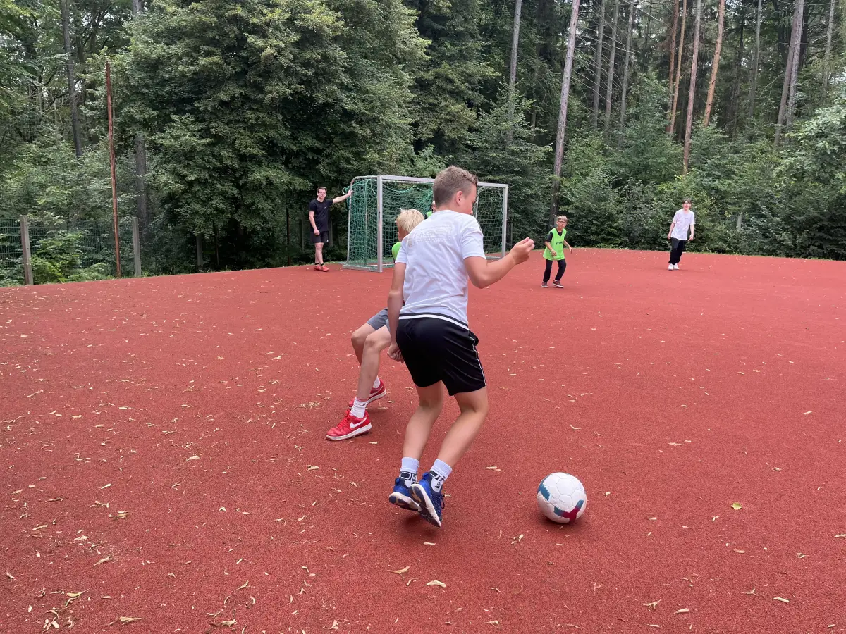 Boys playing football on a red all-weather pitch in the woods