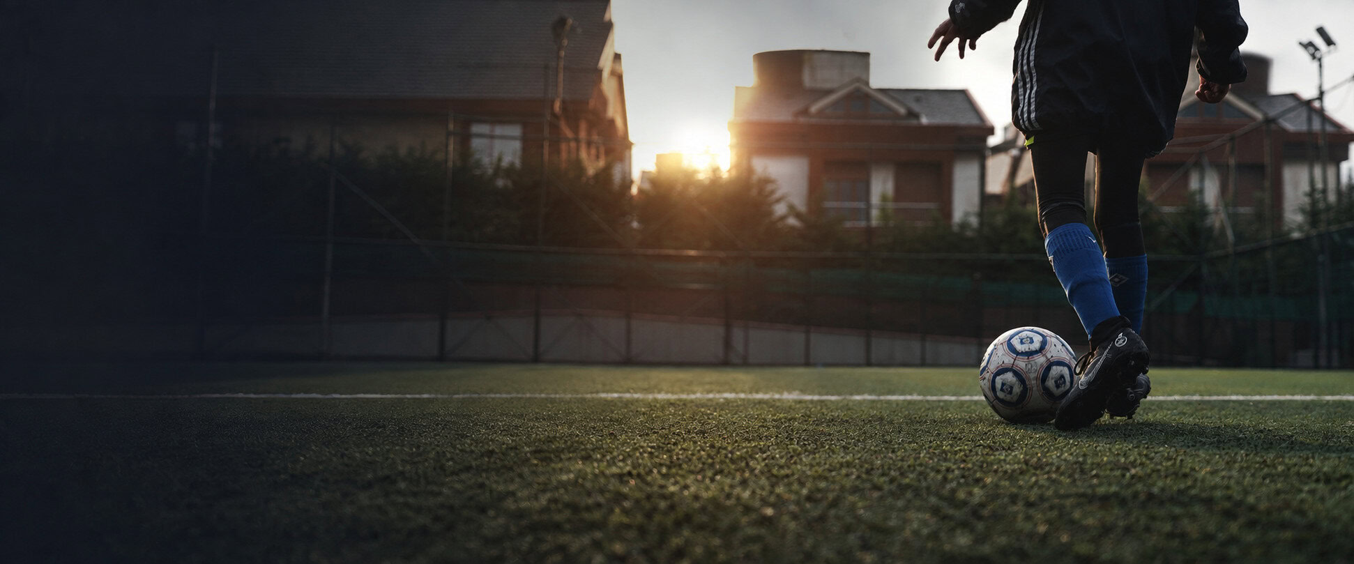 A player’s legs beside a football on a grass pitch at sunset