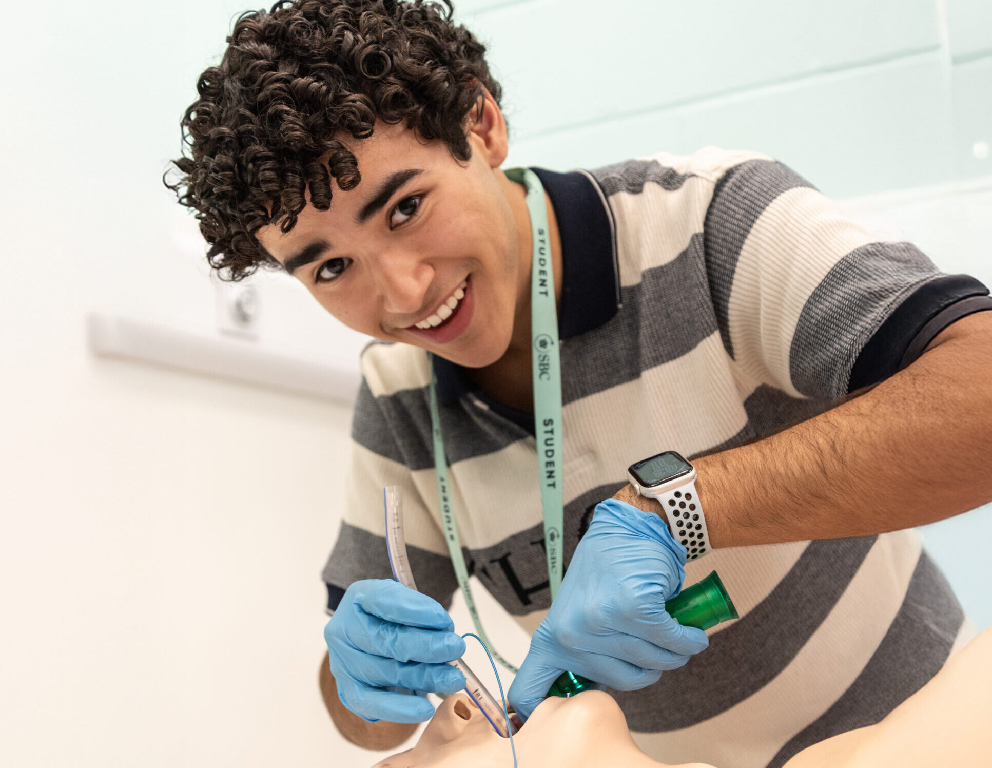 A student in blue gloves smiles while holding a test tube in a lab