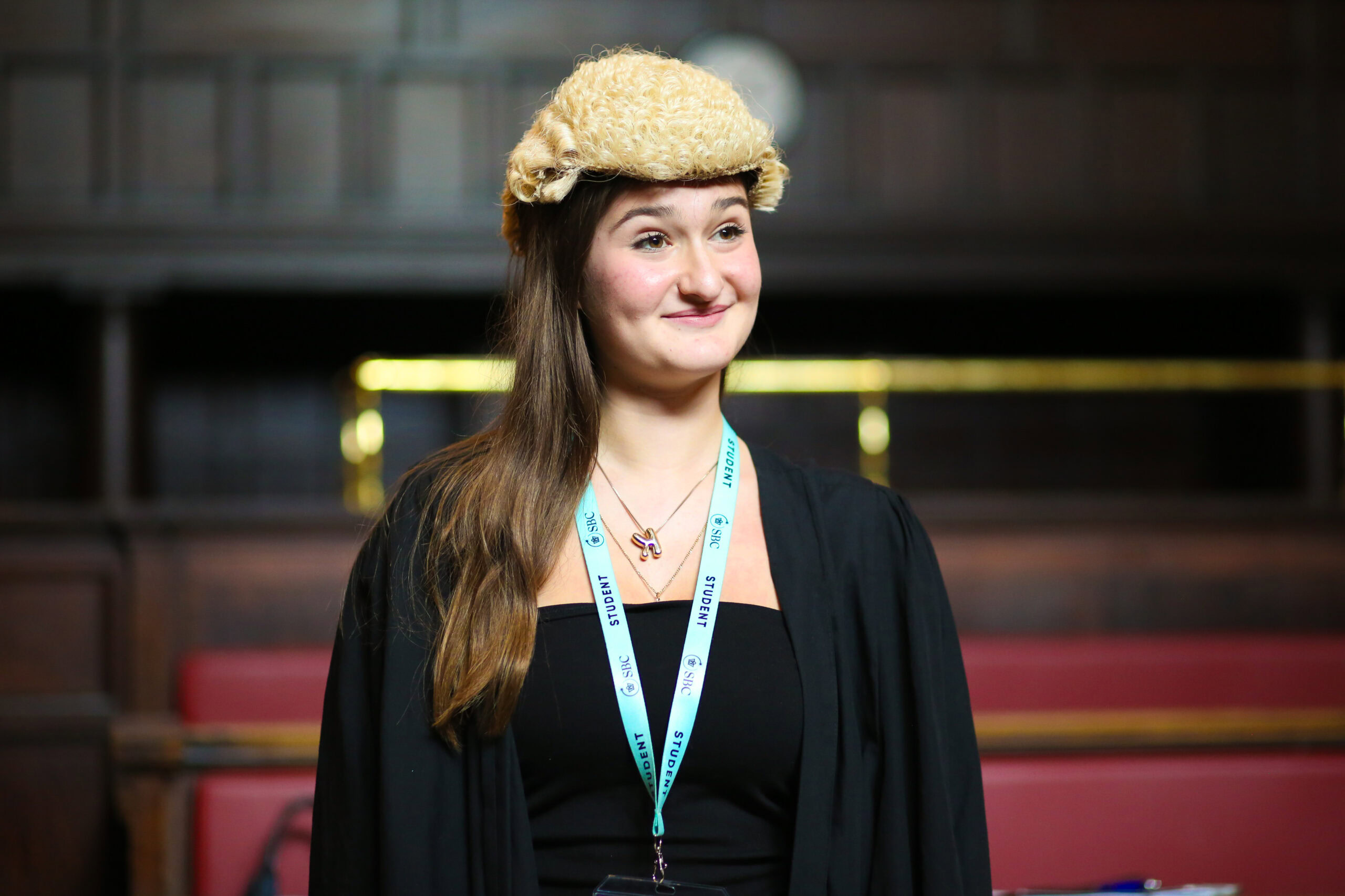 A student wears a gown and cap at a graduation ceremony inside a hall