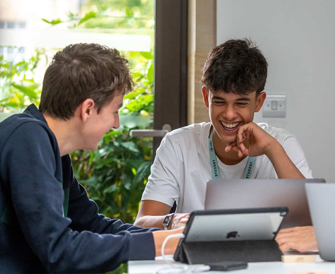 Three students smiling as they work on laptops at the Oxford College programme