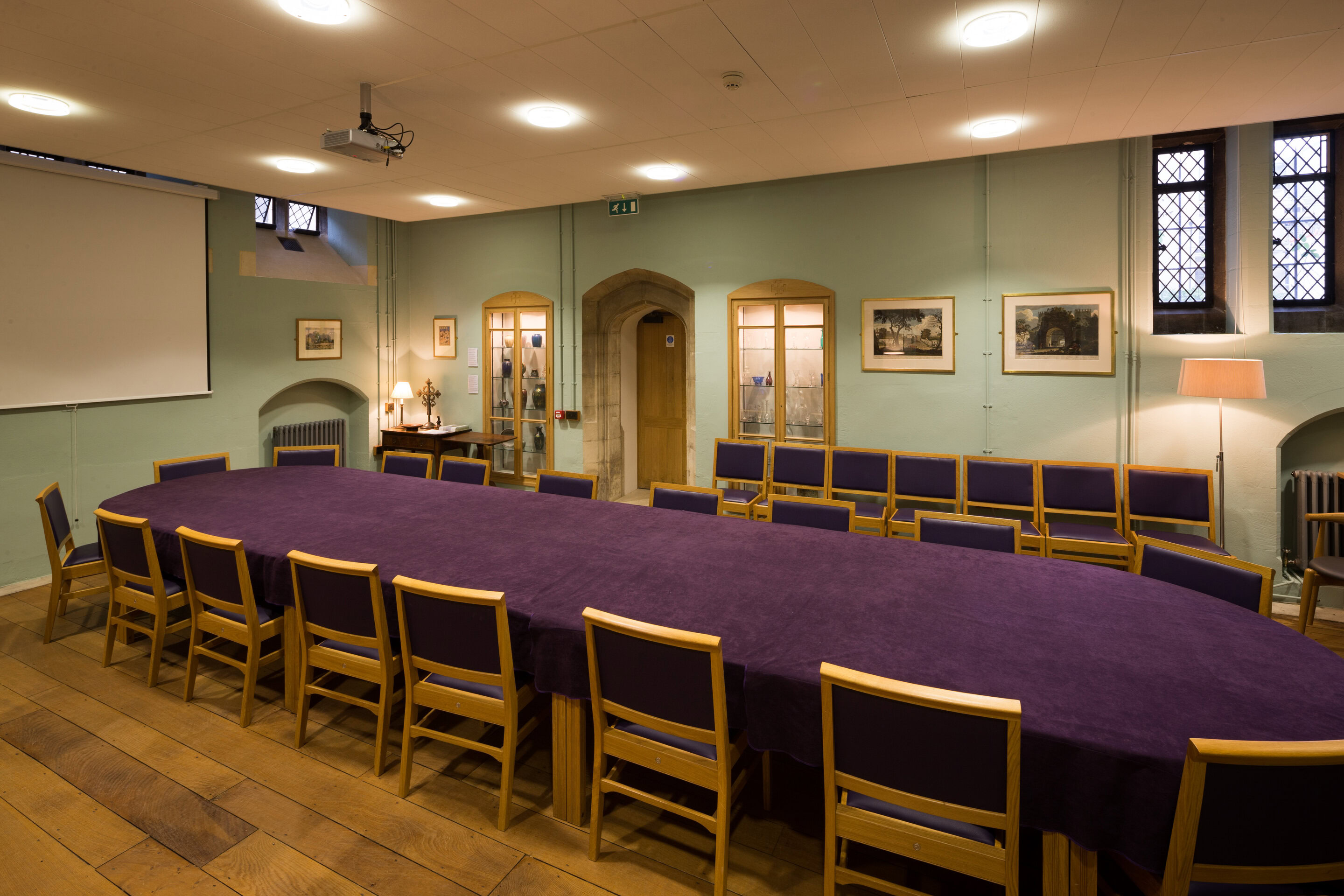 A meeting room with a long purple table, wooden chairs and a projector screen