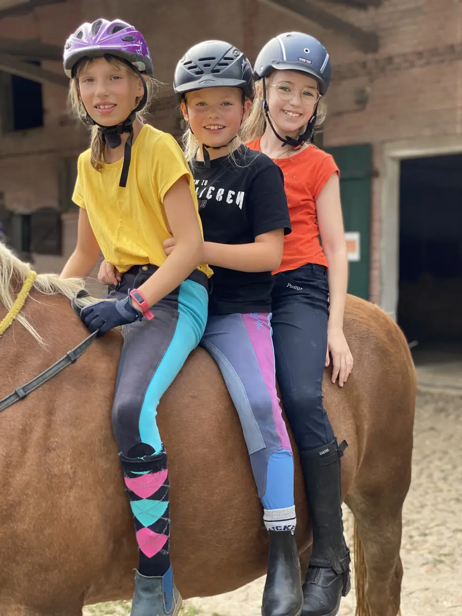Three girls in riding helmets standing beside a chestnut pony in front of the stable at Haflingerhof Kattien