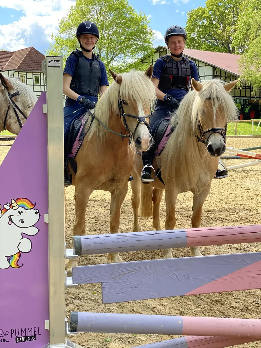 Two riders in helmets and body protectors on Haflinger ponies on the outdoor arena at Haflingerhof Kattien