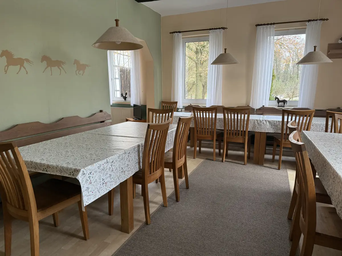 The dining room at Haflingerhof Kattien with long wooden tables and chairs and windows onto the yard