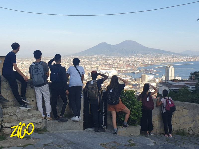 Group of teenagers standing on a wall looking out over Naples with Vesuvius in the distance