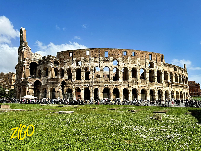 The outer arcades of the Colosseum in Rome seen across a green lawn