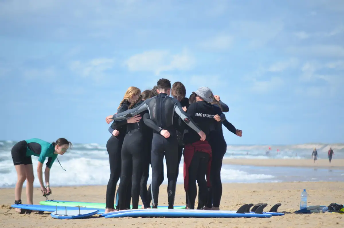 Surf group in wetsuits huddling on the beach beside their boards