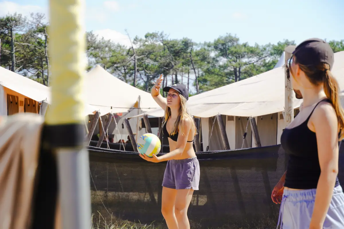 Two girls passing a ball in front of the large canvas sleeping tents