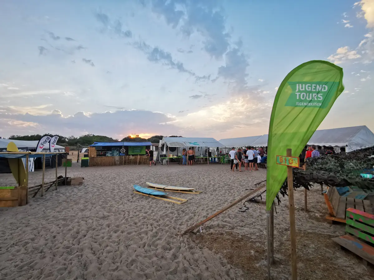 Sandy camp area with marquees and a Jugendtours flag behind the dune at Le Pin Sec