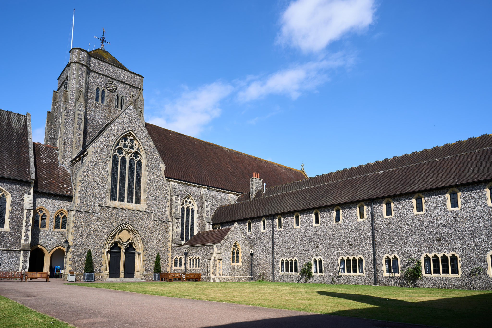 The flint-and-stone chapel and cloister buildings of Hurst College, Hurstpierpoint, under a blue sky