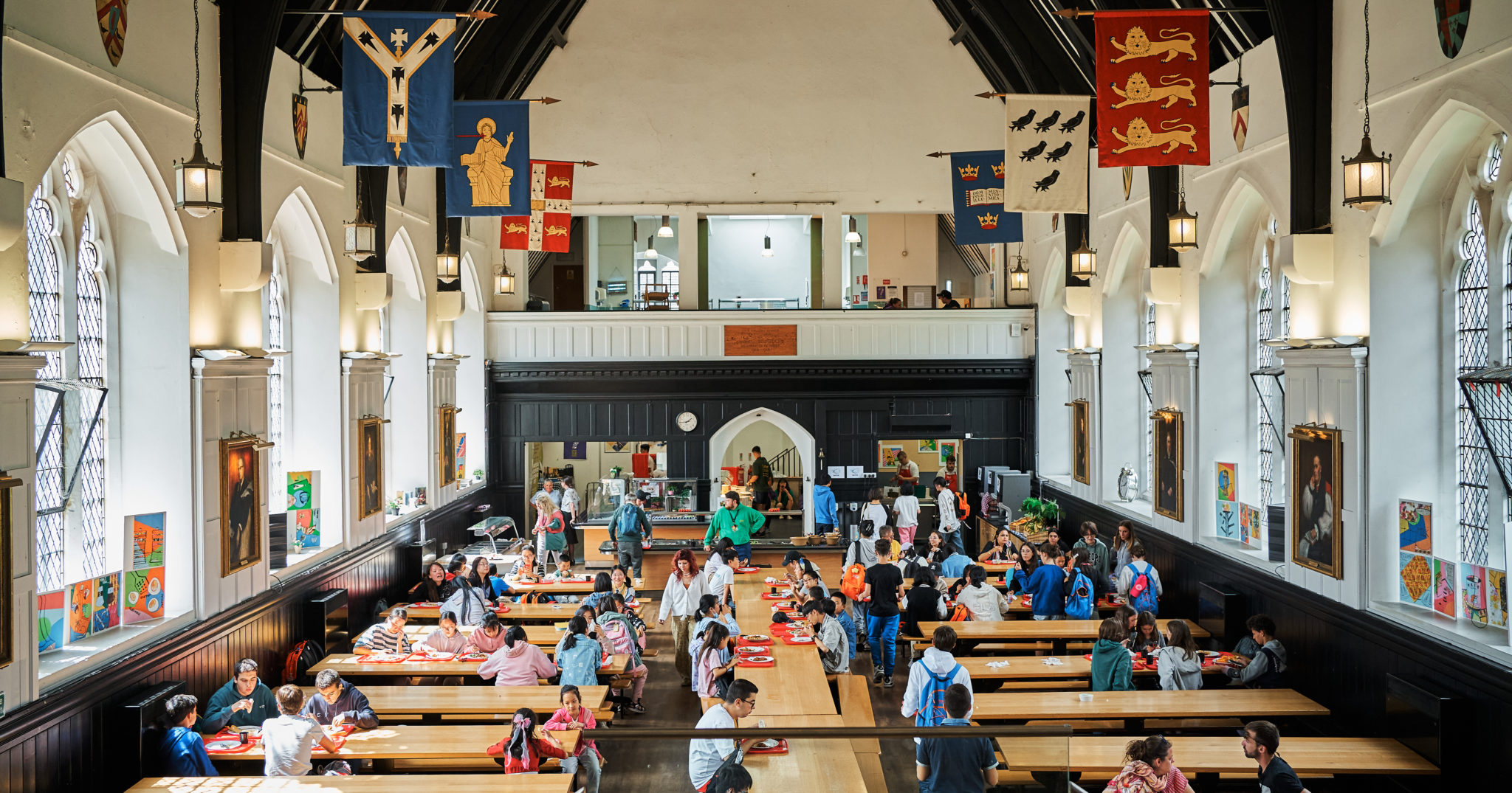 Students eating in the high-ceilinged dining hall with heraldic banners at Hurst College