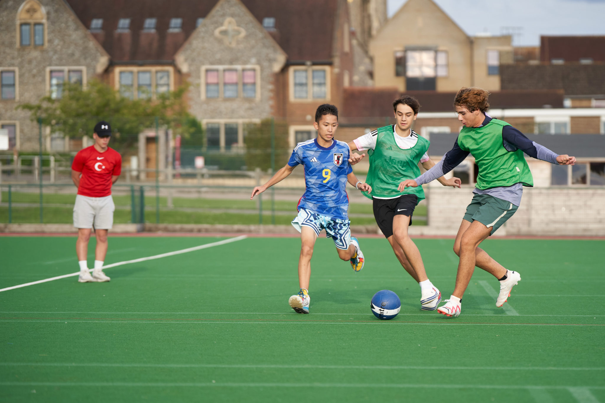 Students playing football on the artificial pitch in front of Hurst College buildings