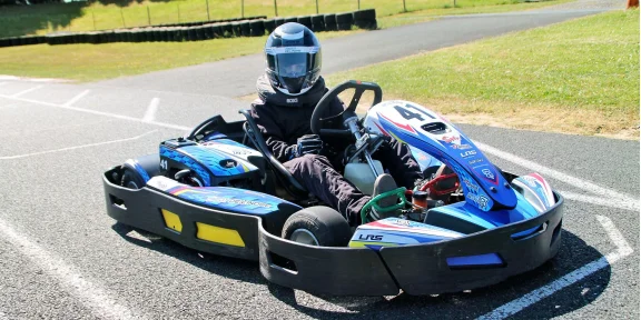 Young driver in helmet and race suit at the wheel of a blue go-kart on the track