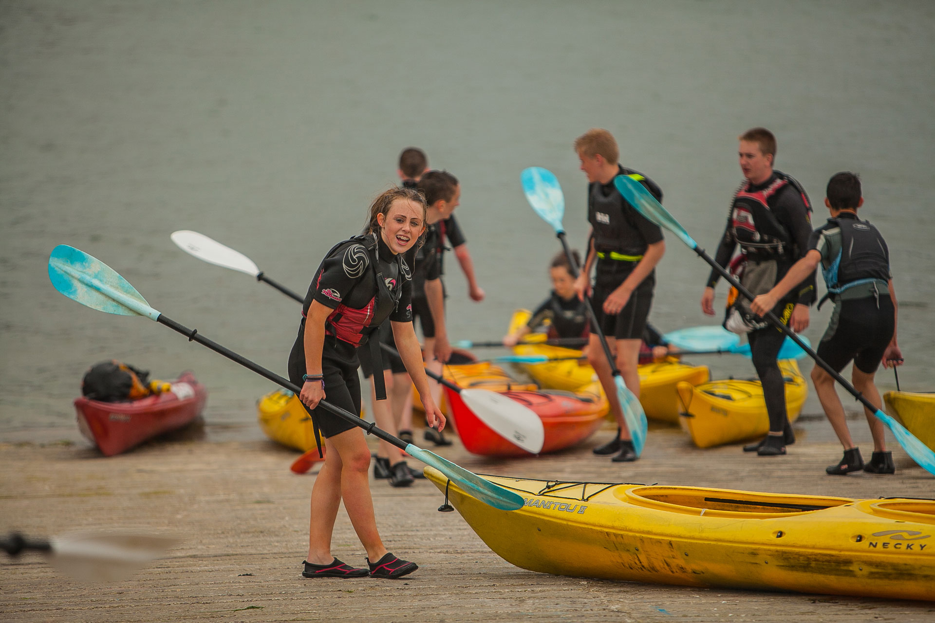 Students in buoyancy aids handling sea kayaks at the water’s edge