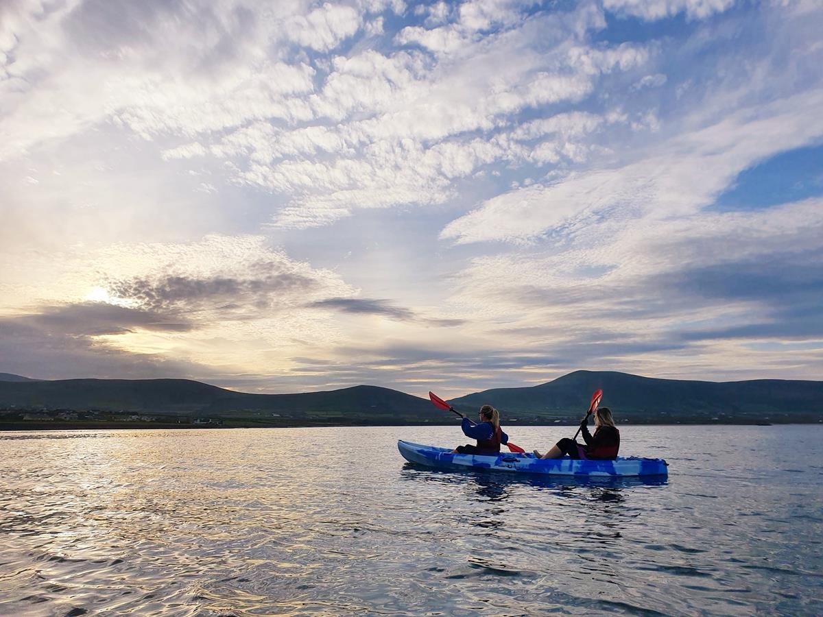 A kayak on calm water at dusk with the bay and hills of the Dingle Peninsula behind