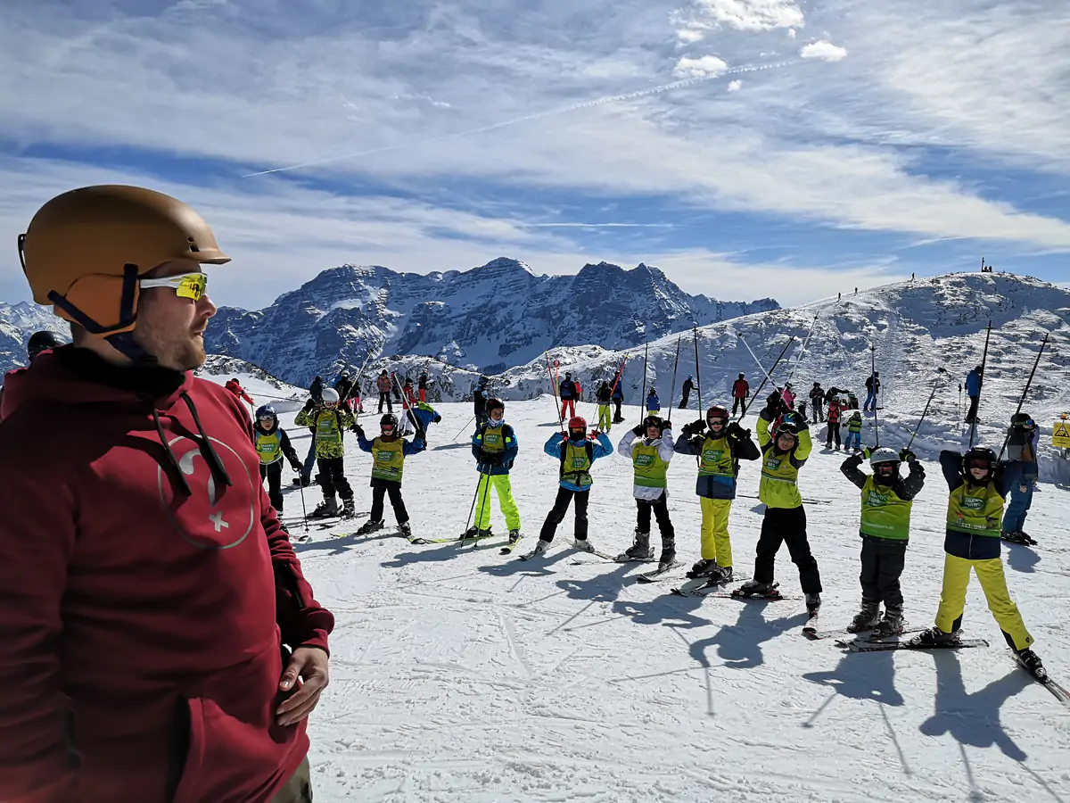 Group of participants in ski gear lined up on the piste with an instructor, mountains behind