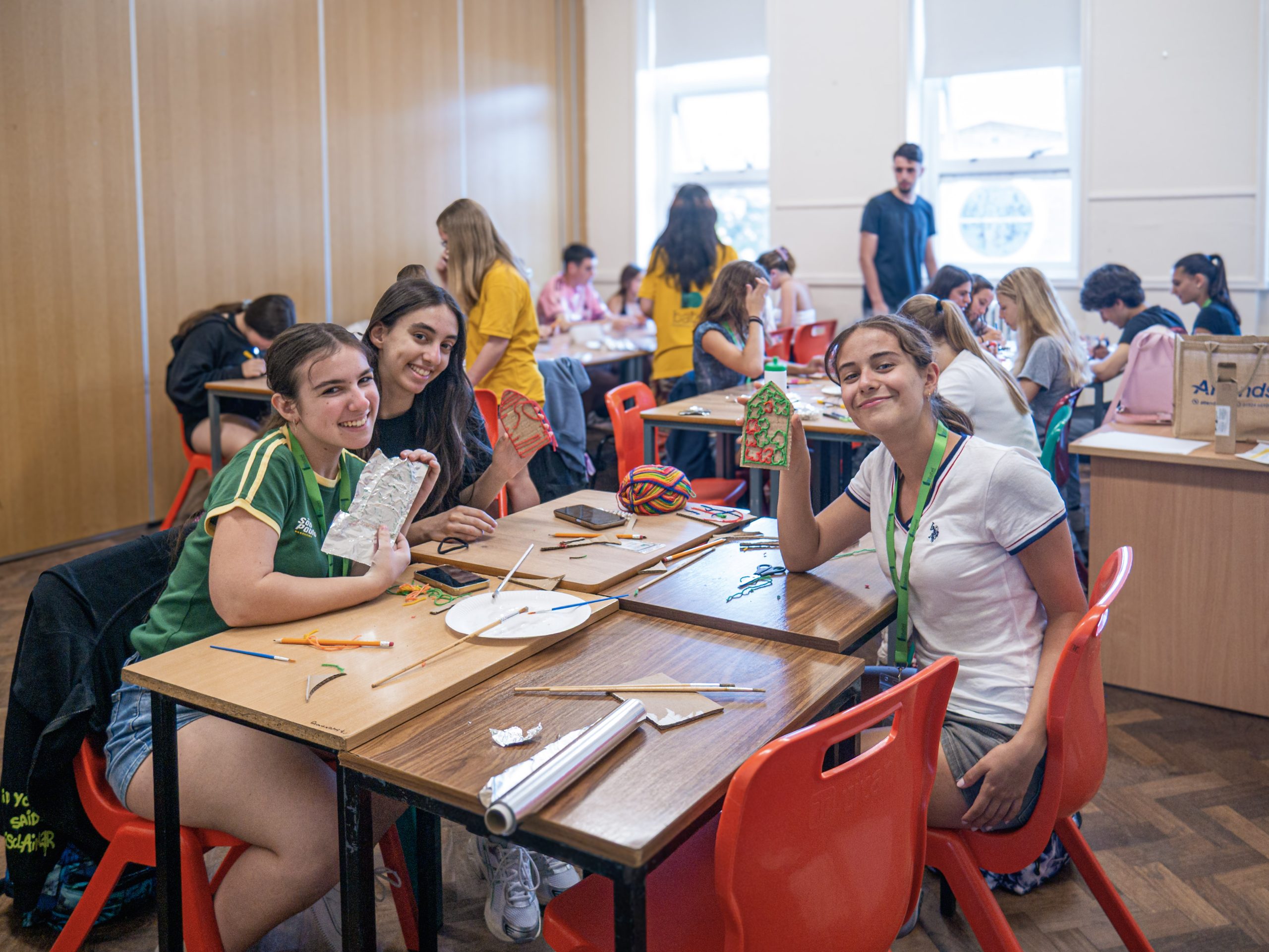 Students at classroom tables making crafts, some holding up their work, during an arts and crafts session at Manor House, Raheny