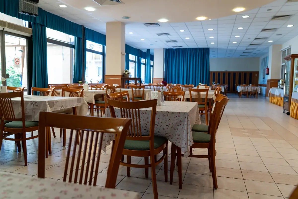 The dining room of the holiday complex with laid tables, wooden chairs and large curtained windows