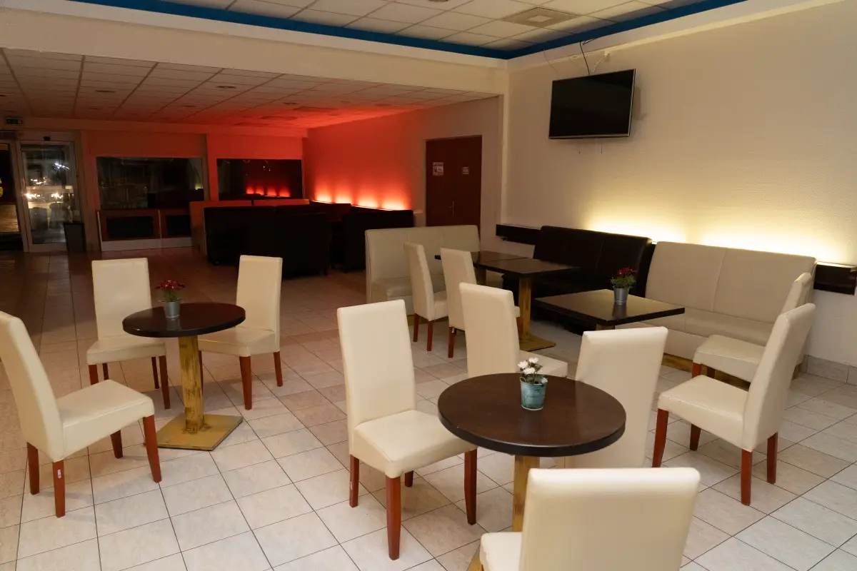 An indoor lounge and bar area with armchairs, low tables and a wall-mounted screen