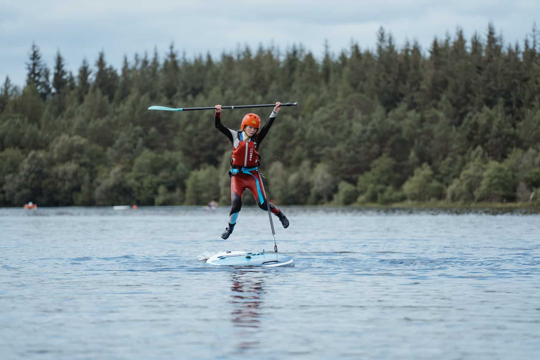 Camper jumping from a stand-up paddleboard on the water, Abernethy Nethy Bridge, Cairngorms National Park