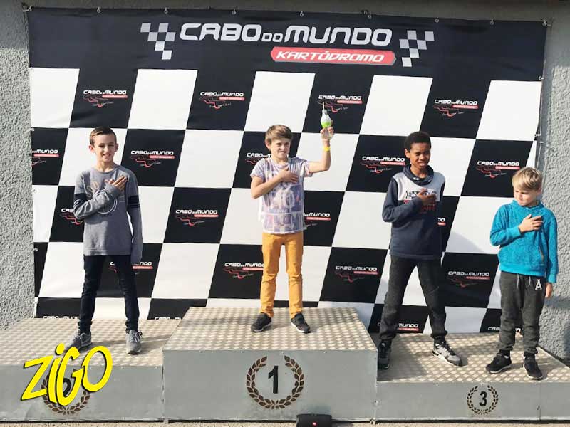 Three participants in racing overalls standing on the numbered podium of the karting circuit