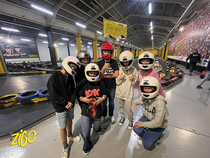 Participants in helmets standing at the edge of an indoor karting track