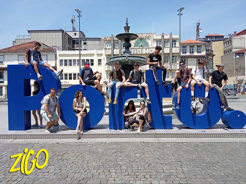 Group of young people climbing on the large blue Porto letters on a city square