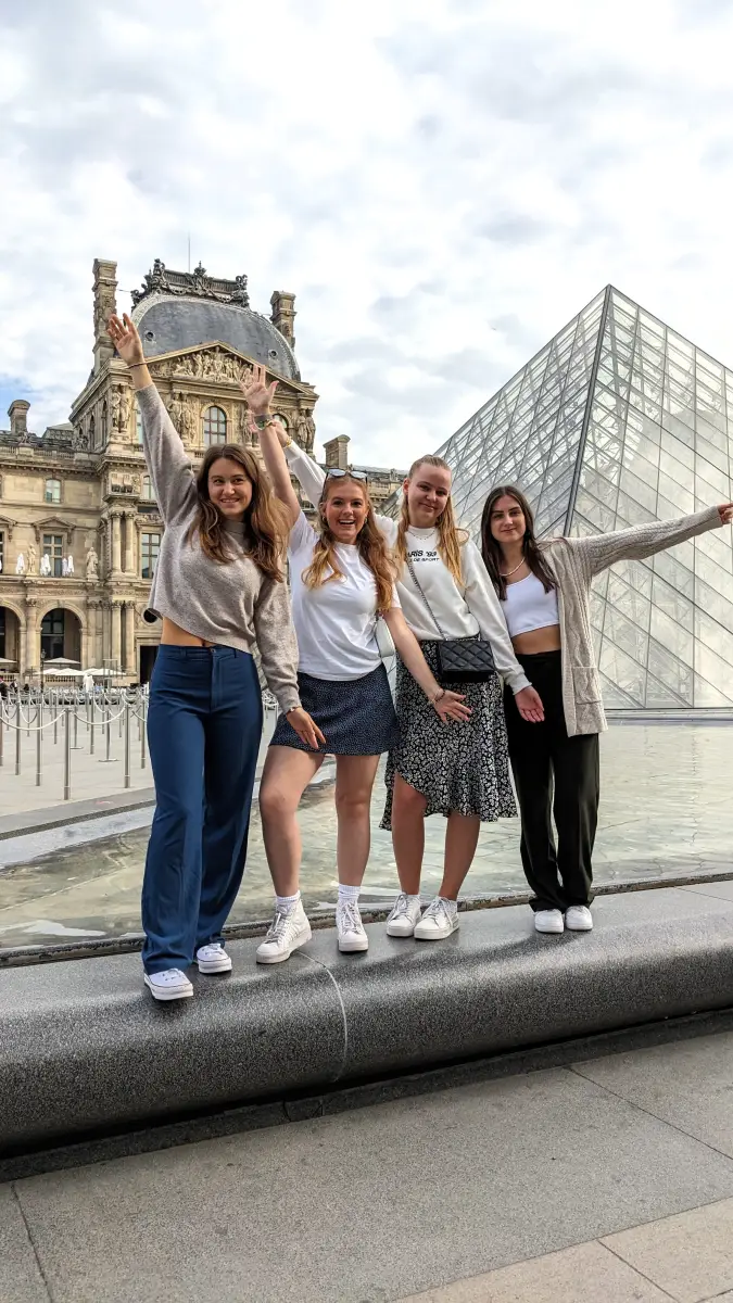 Four young travellers posing beside the glass pyramid in the Louvre courtyard