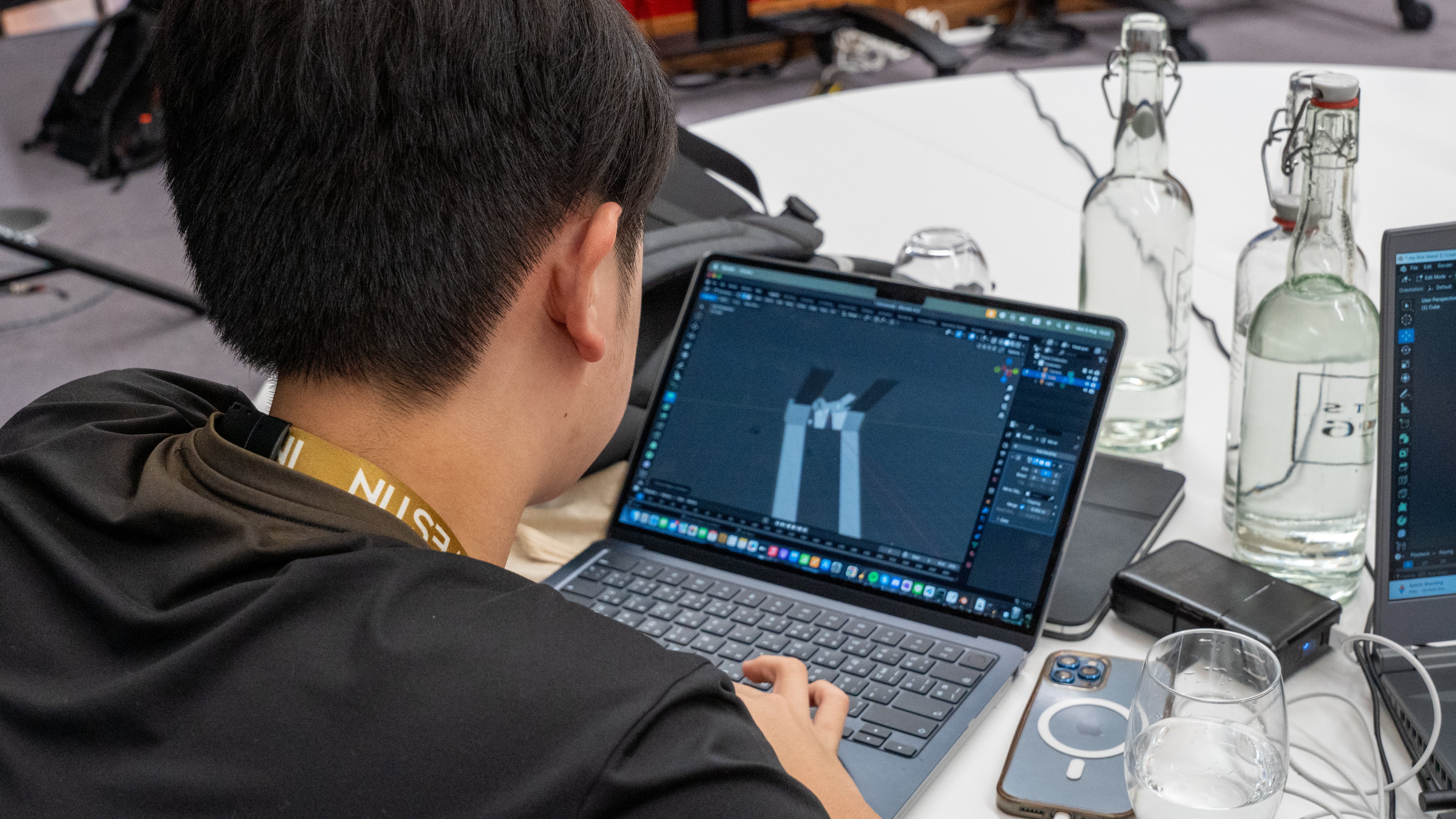 Student with an InvestIN lanyard building a 3D model in Blender on a laptop, InvestIN AI & Software Summer Experience in London
