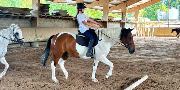 Young rider trotting a piebald pony in the covered riding arena