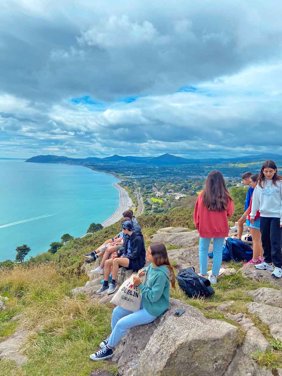 Camp students sitting on a clifftop above a long sandy bay and headland during a full-day weekend tour