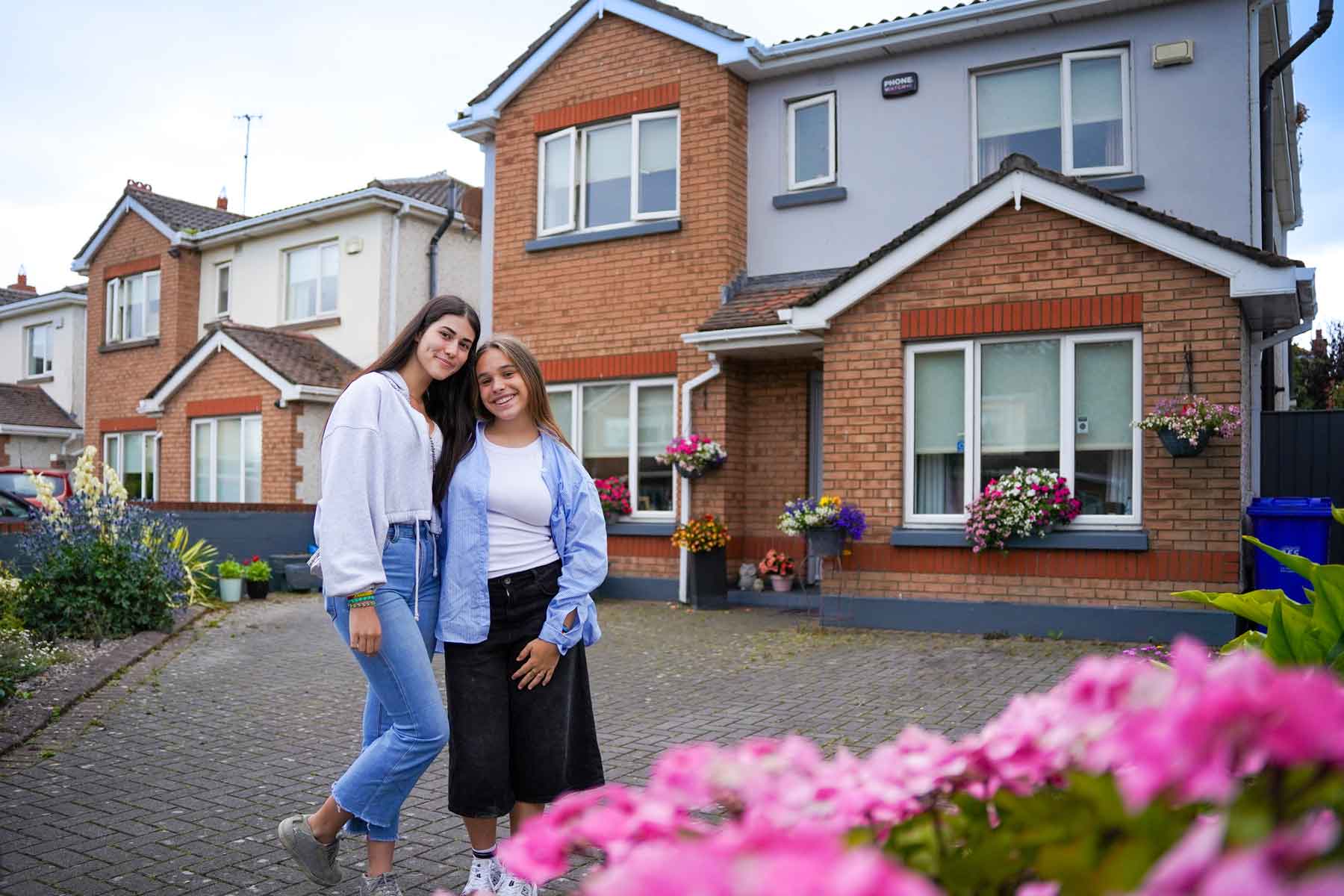 Two camp students standing outside the red-brick host family house where they stay