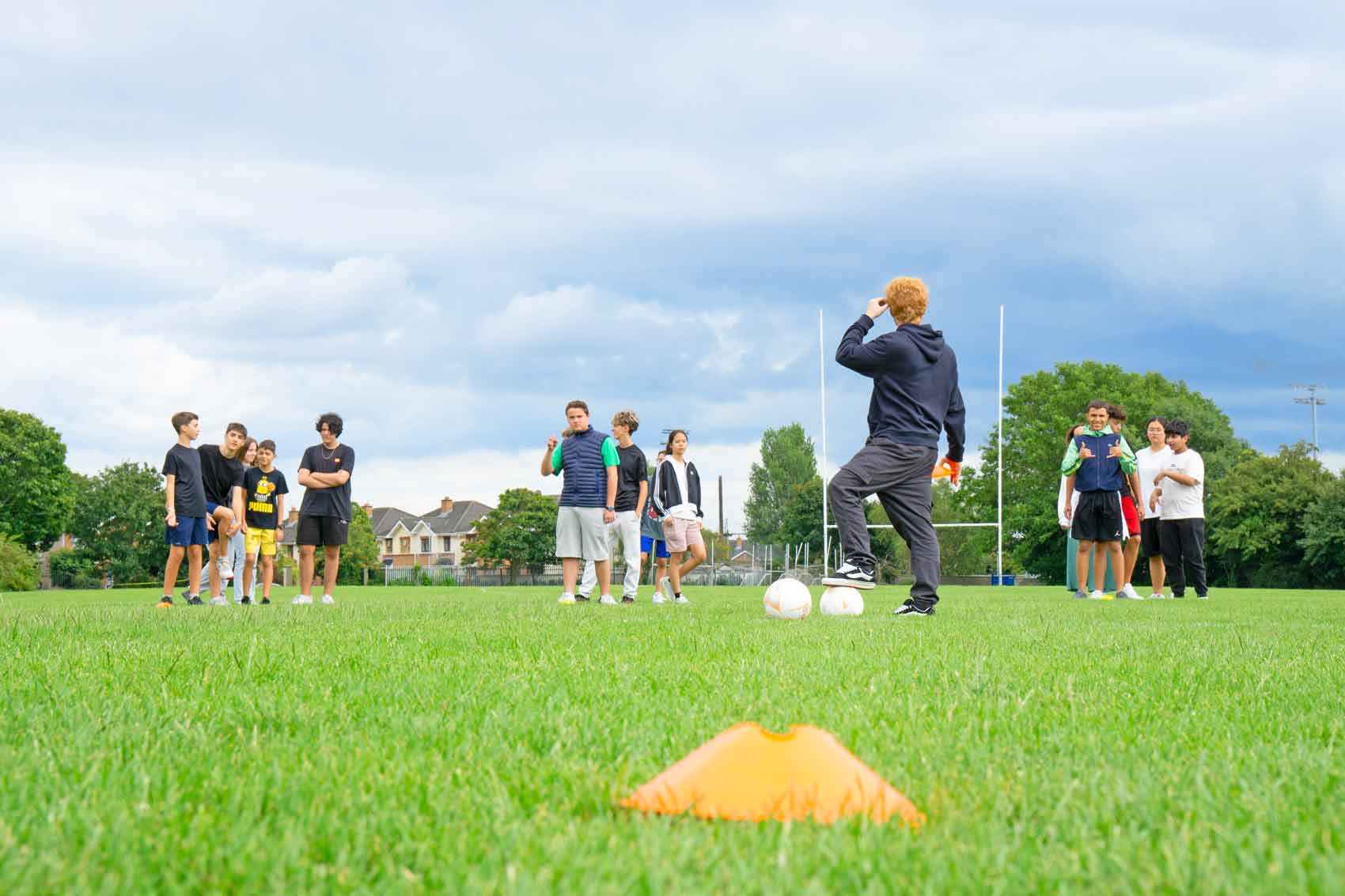 Camp students playing football on a grass pitch with rugby posts behind during an afternoon sports session