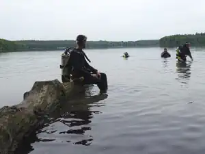 Diver sitting on a rock in Lake Stechlin with other divers in the water