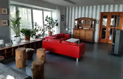 Common room with red sofa, tree-stump seats and large windows at Villa Frida