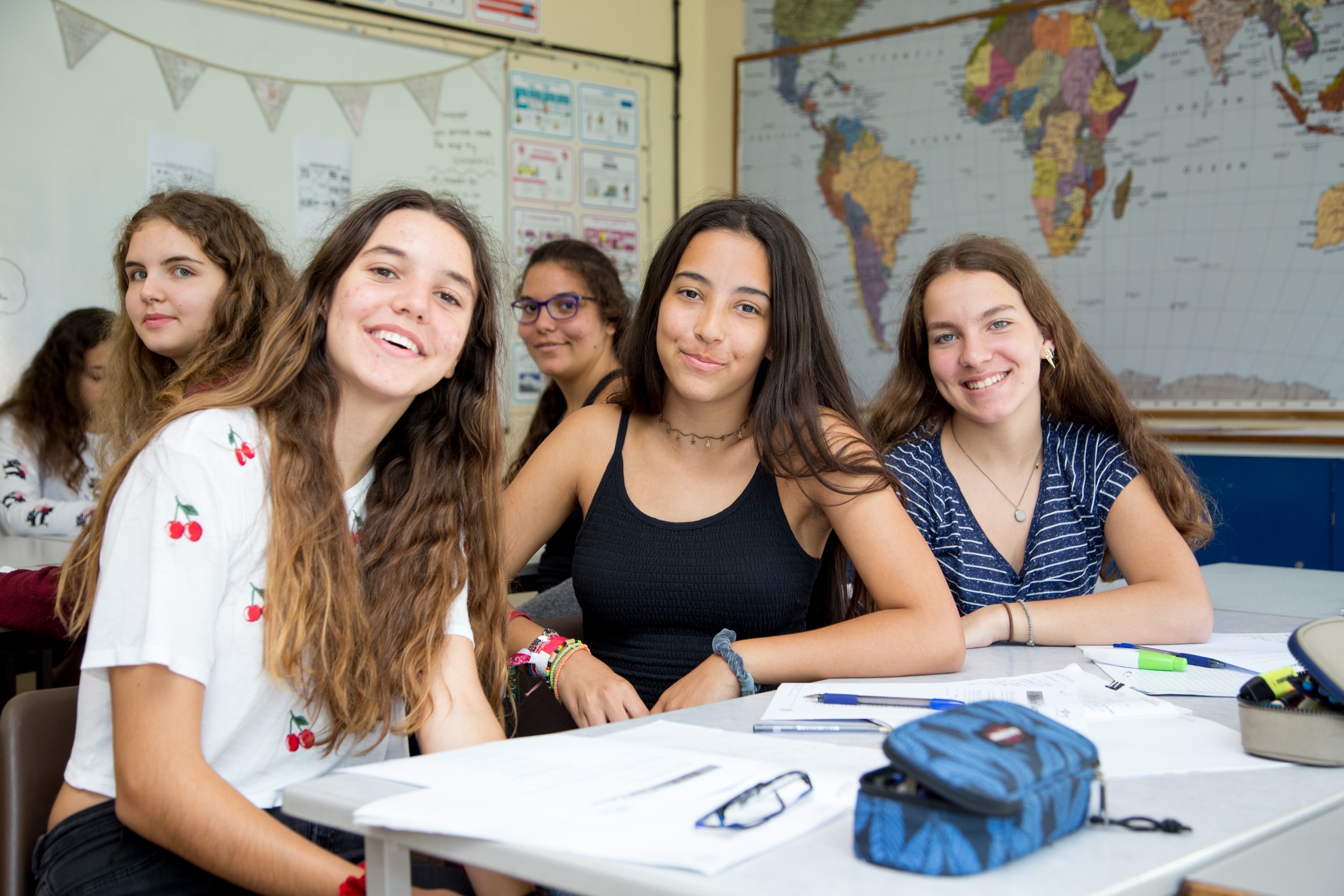 Group of students working together around a classroom table with a world map on the wall