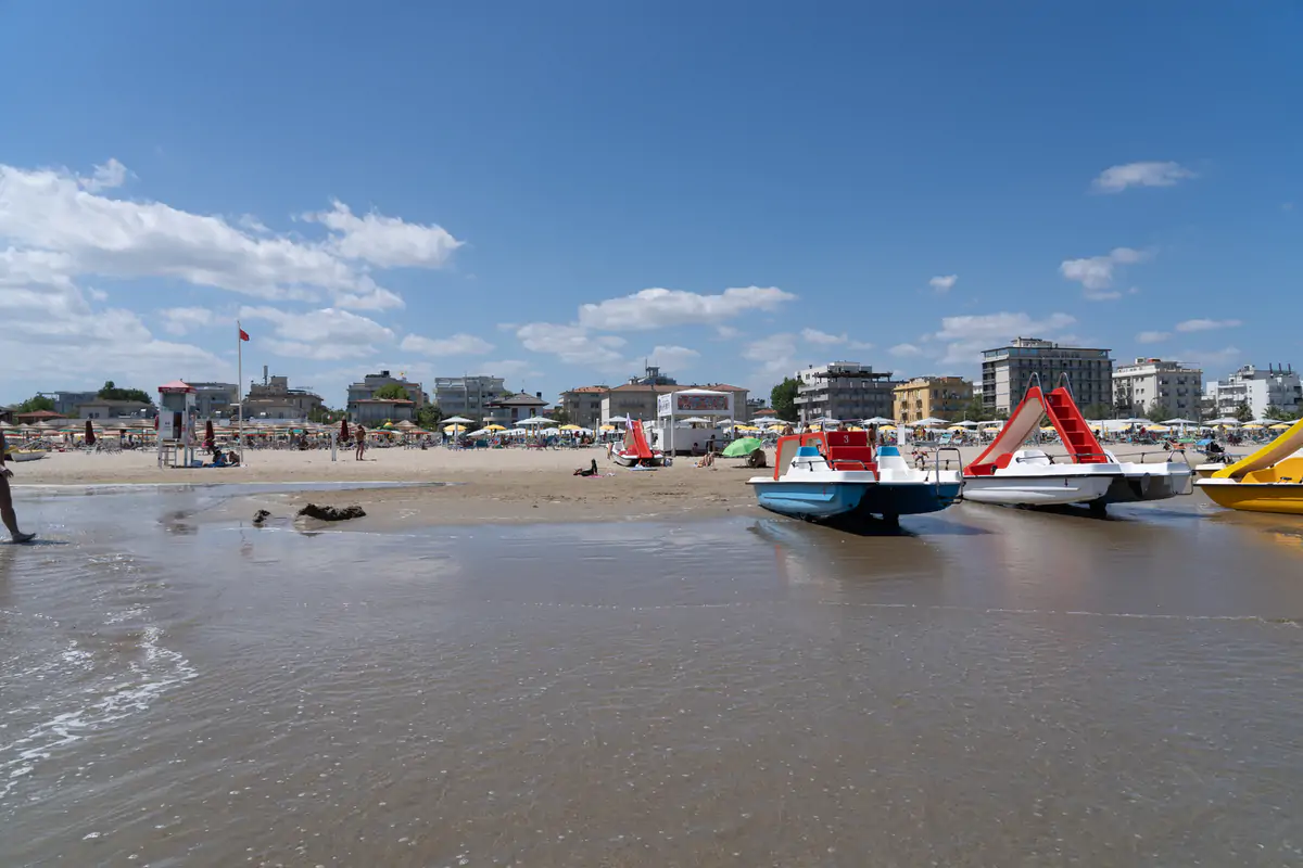 The wide sand beach at Rimini with pedalos drawn up at the shoreline and the seafront buildings behind