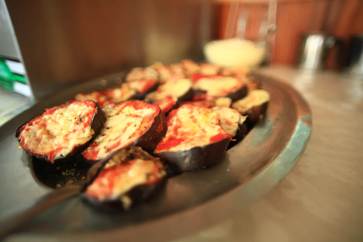 A plate of baked aubergine slices topped with tomato and cheese